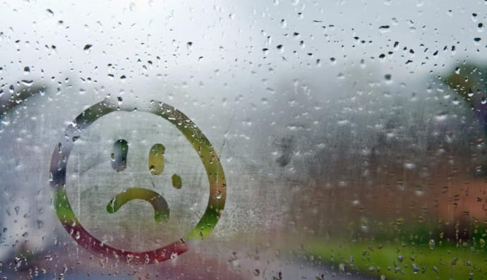 Намальований смайлик на вікні, засмучений через дощ